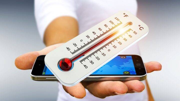 Eine Hand hält ein Smartphone und ein Thermometer